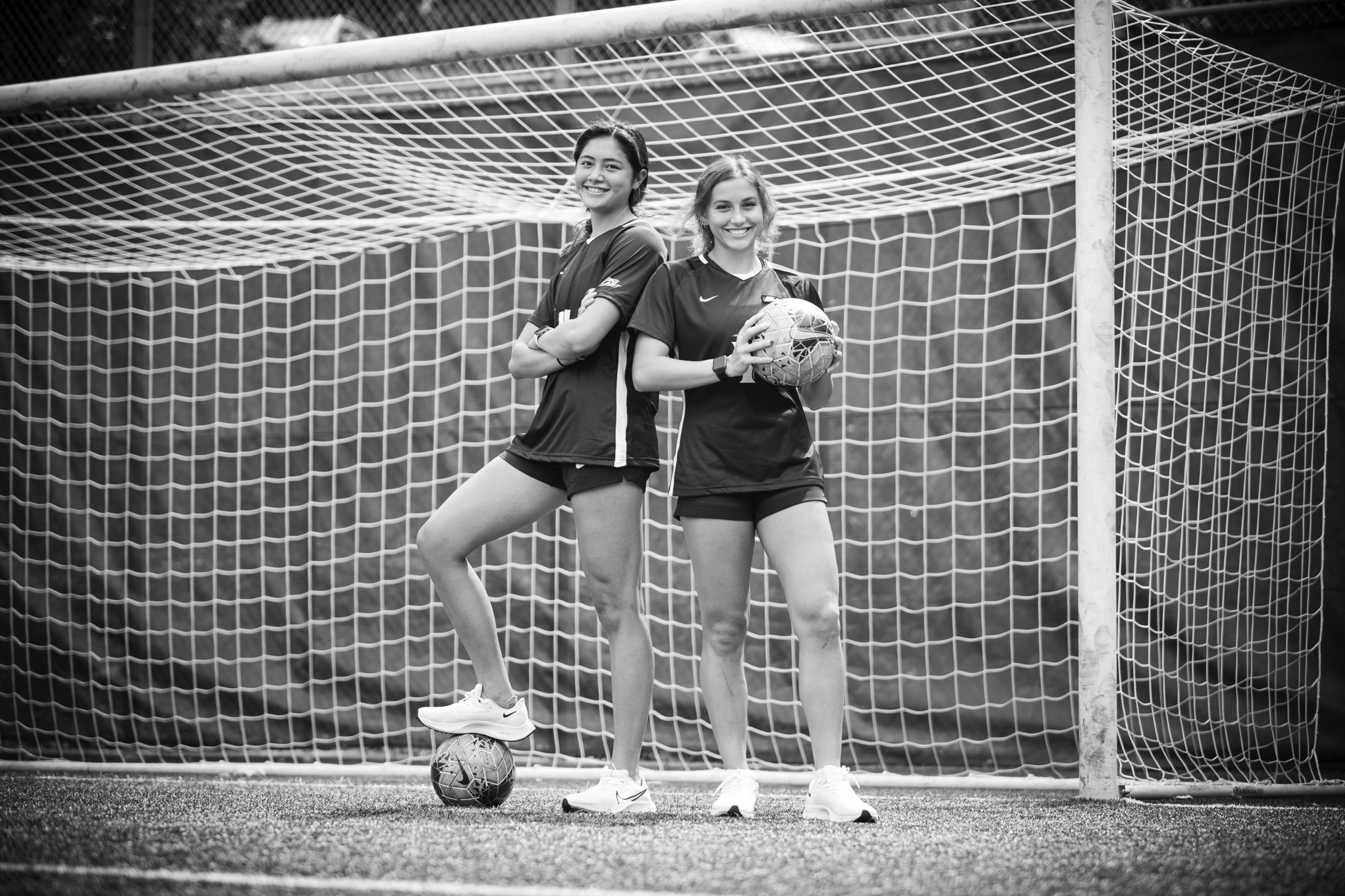 Two women posing in front of a soccer goal.